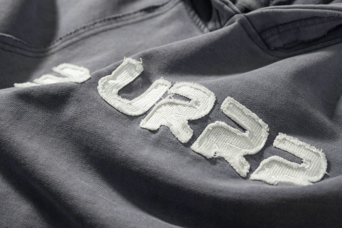 Textured fabric with 'BLURRR' embroidered in white on a dark background