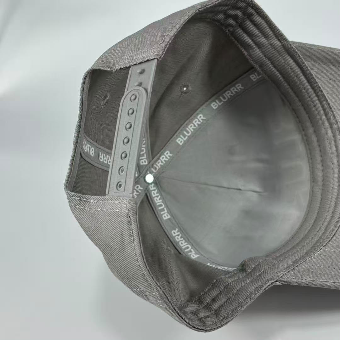 Close-up of the inside of a grey snapback cap, showing the adjustable grey fabric back strap with BLURRR printed repeatedly on it.