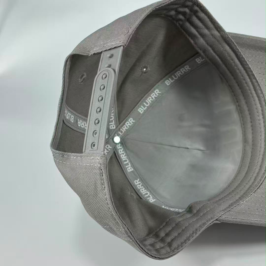 Close-up of the inside of a grey snapback cap, showing the adjustable grey fabric back strap with BLURRR printed repeatedly on it.