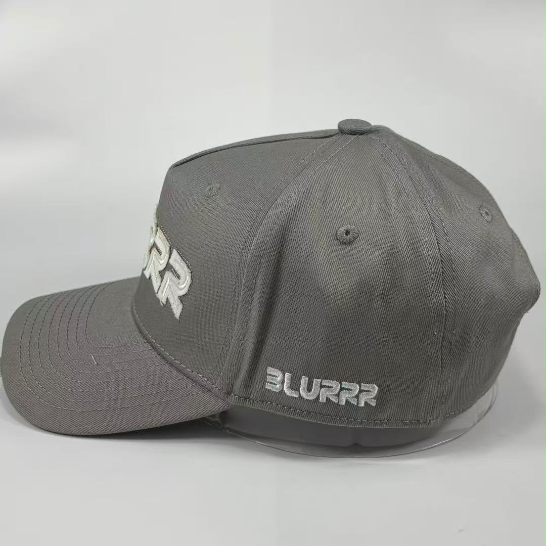 A grey baseball cap with white embroidered 'BLURRR' branding on the side and front, displayed on a clear plastic hanger against a light grey background.