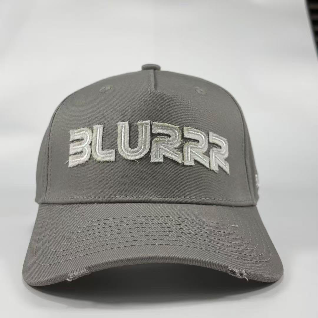 A grey baseball cap with a distressed design, featuring the word 'BLURRR' embroidered in white and grey on the front, set against a plain light grey background.