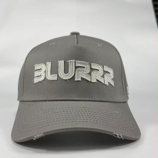 A grey baseball cap with a distressed design, featuring the word 'BLURRR' embroidered in white and grey on the front, set against a plain light grey background.