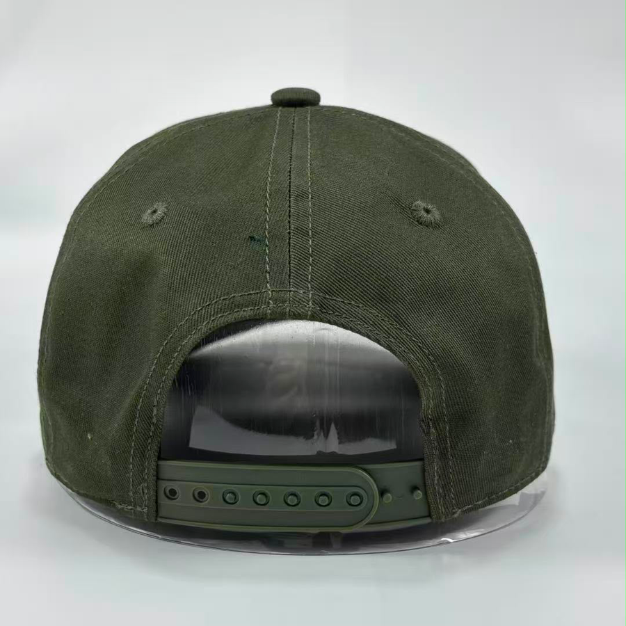 An olive green canvas snapback cap shown from the back, featuring a dark green adjustable strap and a clear plastic display stand against a light gray background.
