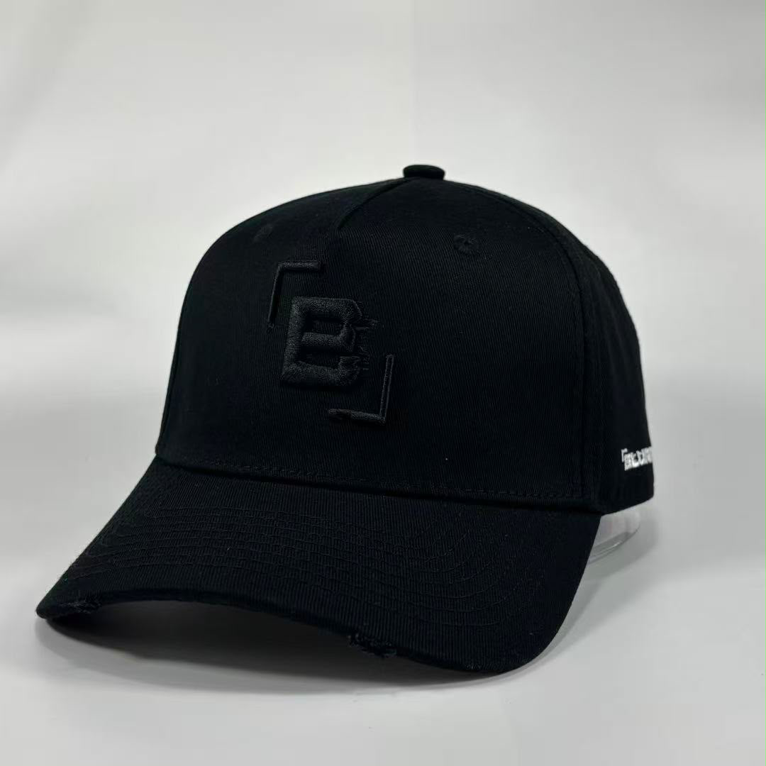 A black baseball cap with a distressed brim, featuring a black embroidered geometric 'B' logo on the front and a small white embroidered logo on the side, photographed on a light grey background.