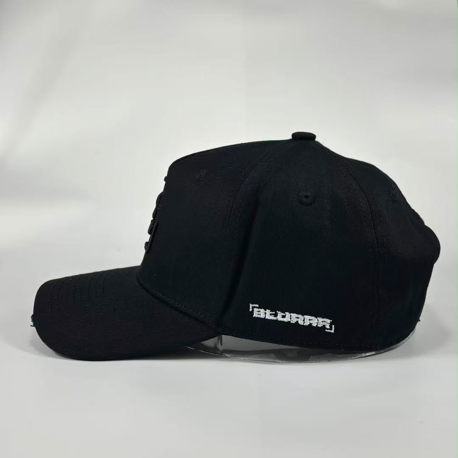 A black baseball cap with a curved brim, featuring a white stylised 'BLURRR' logo on the side, displayed on a clear stand against a light grey background.