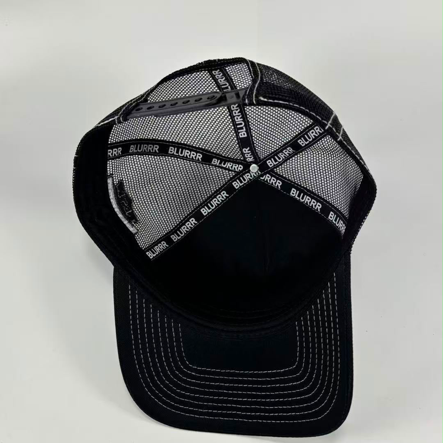 Black trucker-style baseball cap with a black mesh back and white contrast stitching on the visor, photographed on a light gray background.