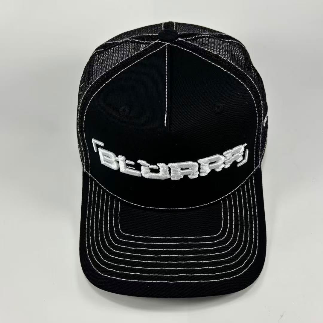 A black trucker-style cap with white contrast stitching and a white embroidered logo reading 'BLURRR' on the front, photographed against a light gray background.
