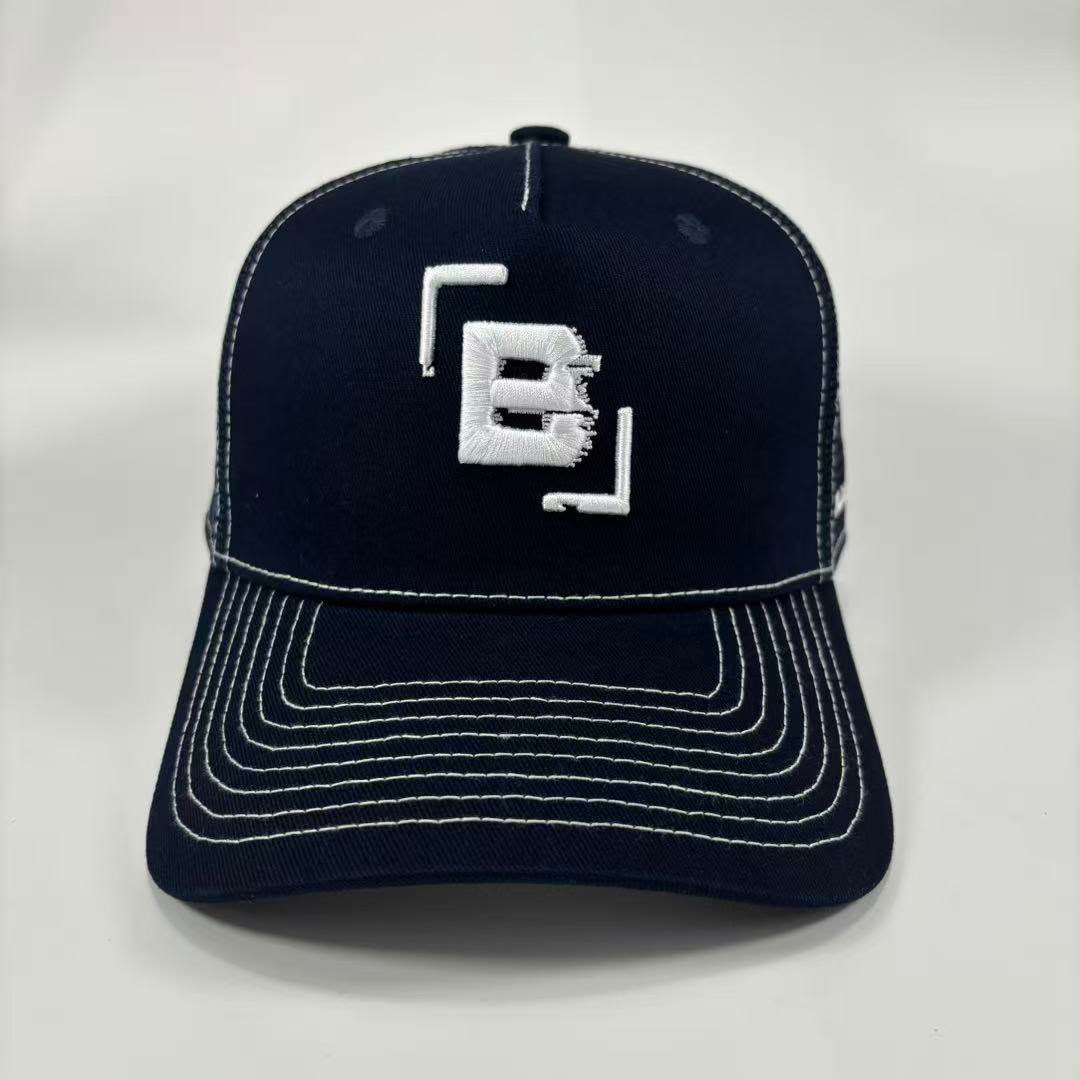 A dark navy blue baseball cap with white contrast stitching and a white embroidered logo on the front, photographed against a light grey background.
