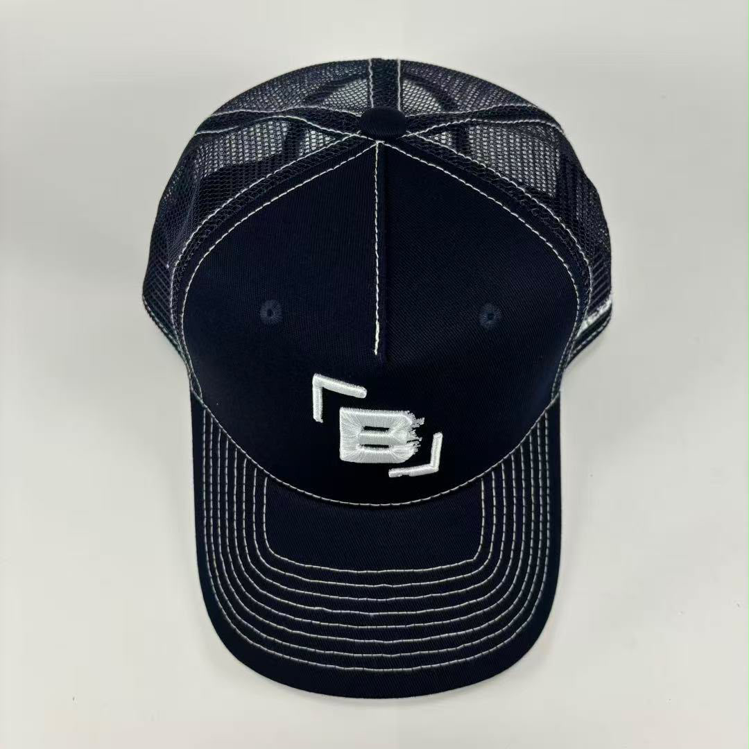 A dark navy blue trucker-style baseball cap with white contrast stitching and a white embroidered logo on the front, shown against a light gray background.