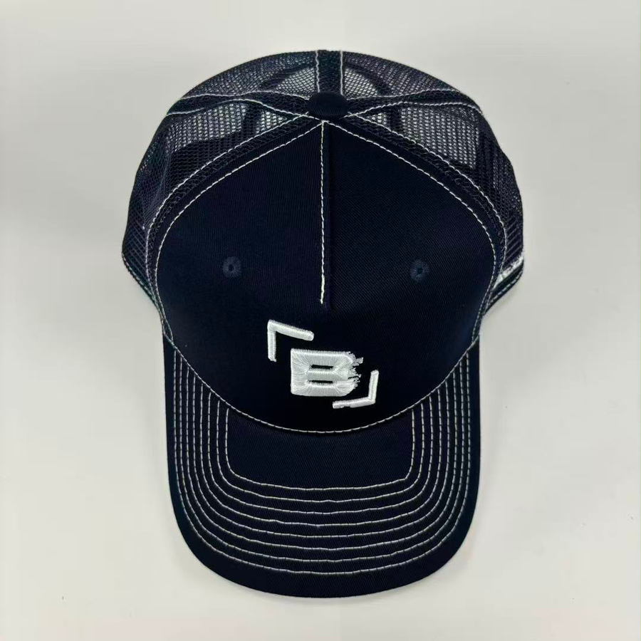 A dark navy blue trucker-style baseball cap with white contrast stitching and a white embroidered logo on the front, shown against a light gray background.