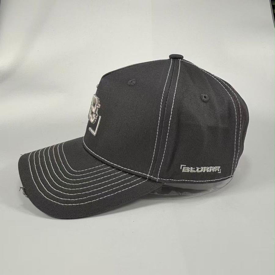 A dark gray baseball cap with white contrast stitching, featuring a small embroidered logo on the side shown against a light gray background.