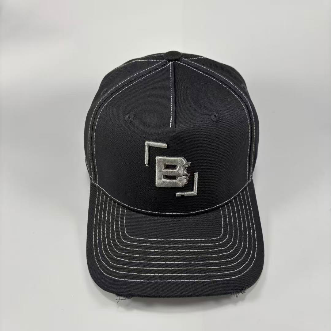 A dark grey baseball cap with white contrast stitching and a silver metallic 'B' logo on the front, photographed against a light grey background.