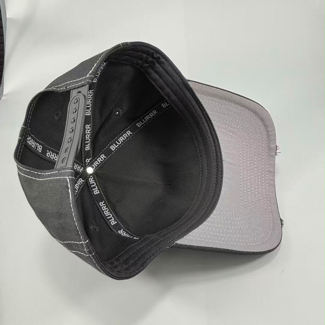 A baseball cap shown from an overhead angle, featuring a black fabric crown with white contrast stitching, a black interior, and a light gray to white visor.