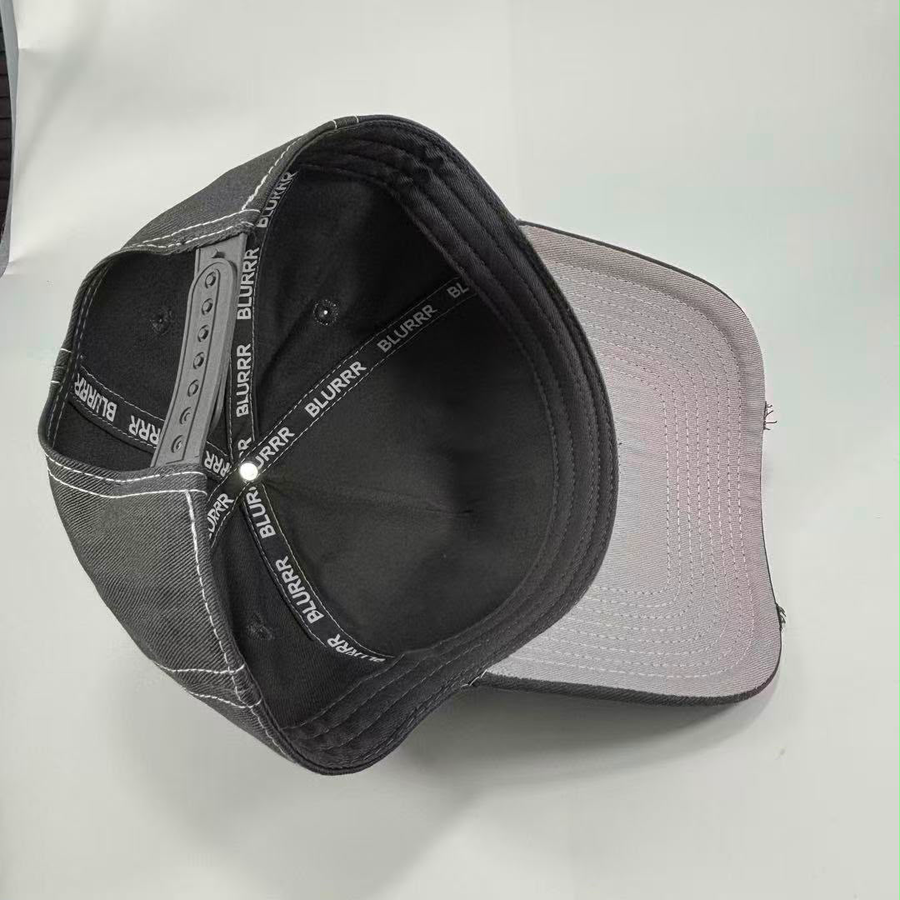 A baseball cap shown from an overhead angle, featuring a black fabric crown with white contrast stitching, a black interior, and a light gray to white visor.