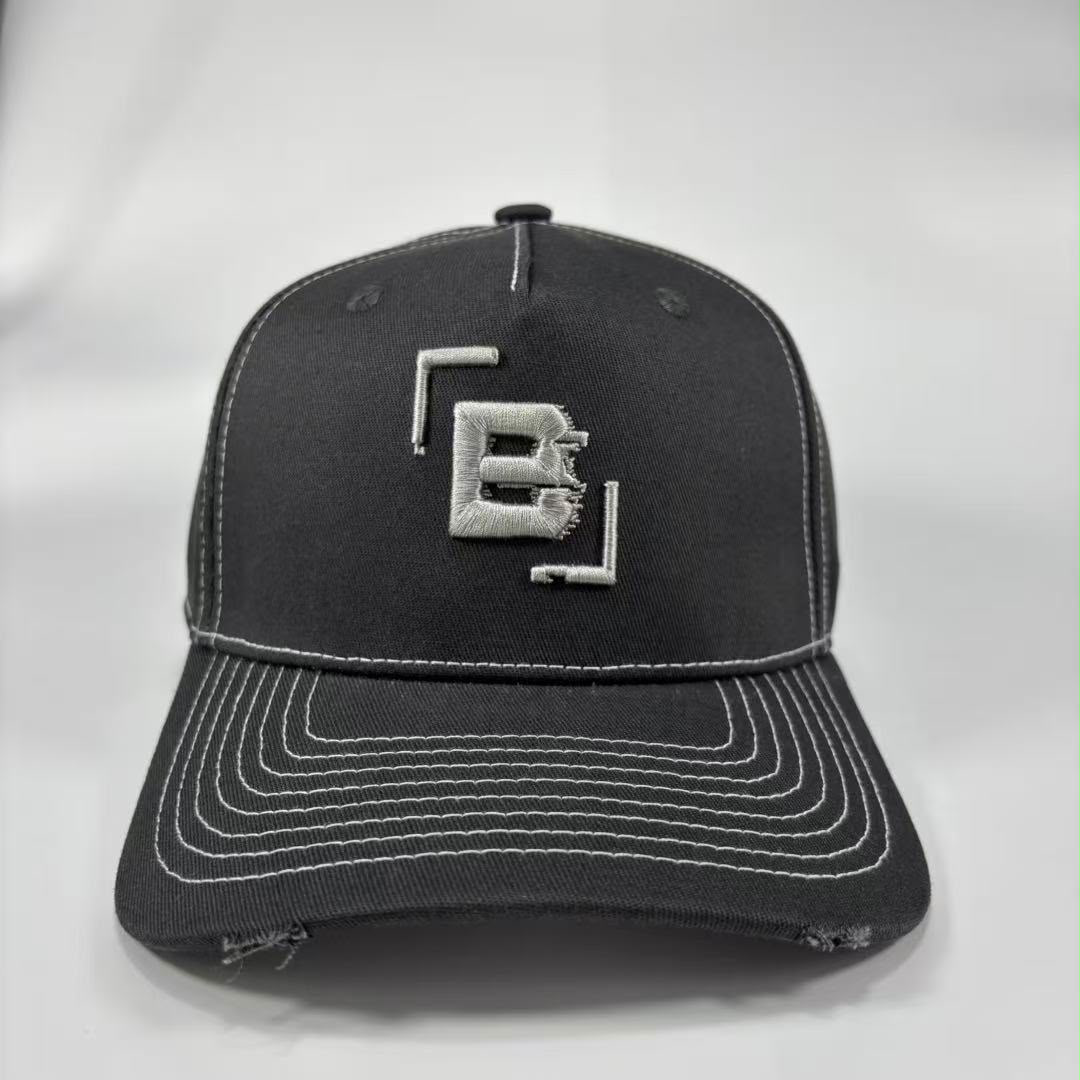 A dark grey baseball cap with distressed detailing on the brim and white contrast stitching, featuring a silver embroidered geometric 'B' logo on the front.