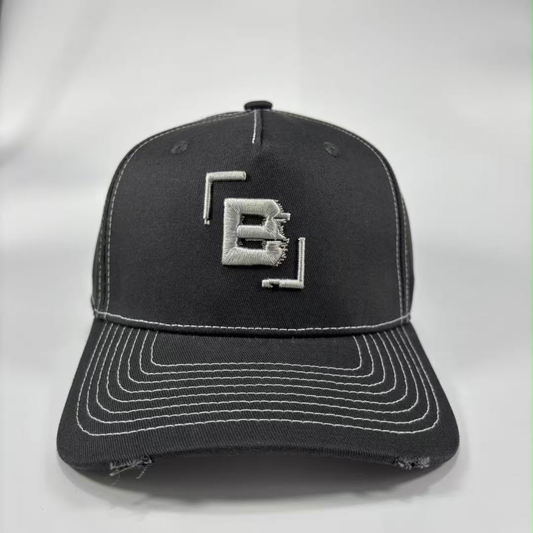 A dark grey baseball cap with distressed detailing on the brim and white contrast stitching, featuring a silver embroidered geometric 'B' logo on the front.
