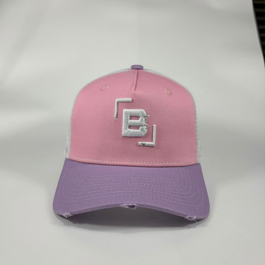 A two-tone trucker-style baseball cap with a pink front panel, lavender-purple brim, and white mesh back. The front panel features a white embroidered geometric 'B' logo.