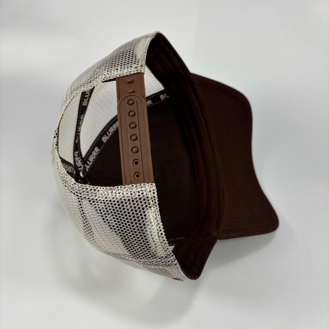 A trucker-style cap shown from an angled top view, featuring a brown visor, brown interior, and a white mesh back with a brown adjustable strap.