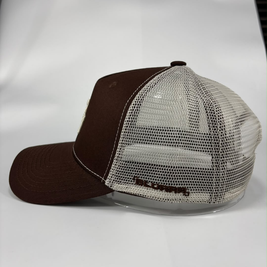 A brown and off-white trucker hat with a solid brown front panel and brim, and an off-white mesh back. The back features embroidered text reading 'BLURRR'.
