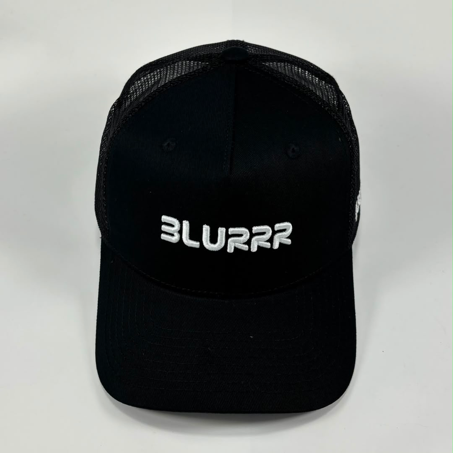 A black trucker-style cap with a curved brim, black mesh back panels, and a white embroidered 'BLURRR' logo on the front, photographed against a light grey background.