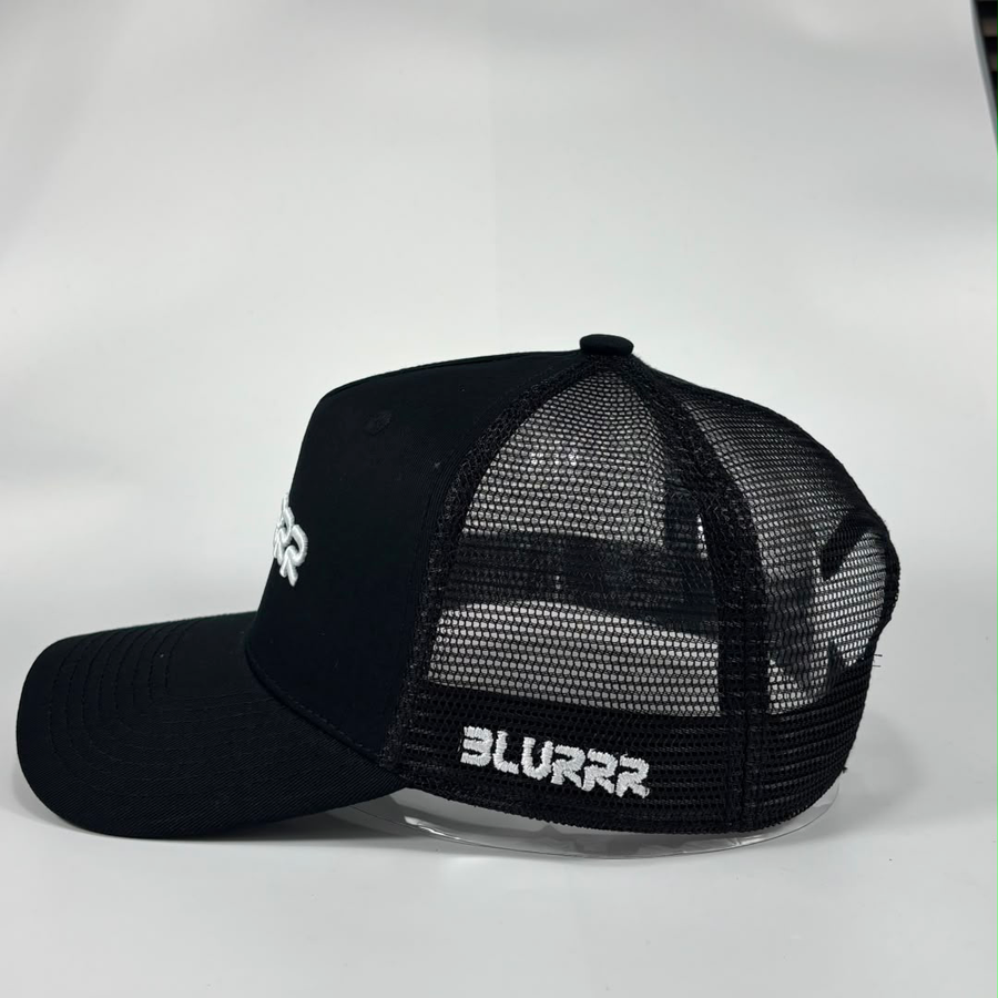 A black trucker-style cap with a curved brim, black mesh back panels, and white embroidered branding. The front panel shows a partial white logo, and the side of the brim reads 'BLURRR' in white.