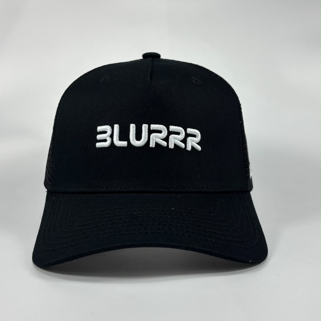 A black trucker-style baseball cap with white embroidered text reading 'BLURRR' on the front, photographed against a light grey studio background.